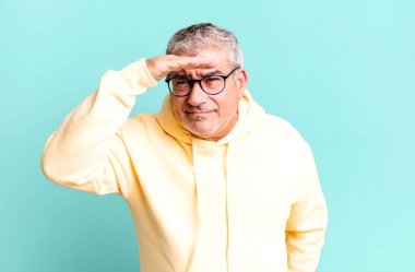 Orta yaşlı bir adam şaşkınlık ve şaşkınlık içinde bakıyor, alnının üstünden bakıyor, izliyor ya da arıyor.