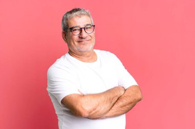 Orta yaşlı bir adam kollarını kavuşturup mutlu bir şekilde gülüyor, rahat, pozitif ve tatmin edici bir pozla.