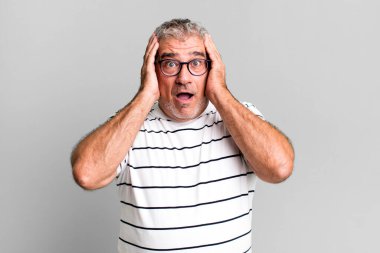 Orta yaşlı bir adam mutsuz, korkmuş ya da endişeli görünüyor ağzı sonuna kadar açık ve iki kulağını da elleriyle kapatıyor.