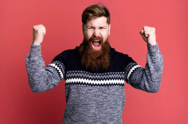 Uzun sakallı ve kızıl saçlı adam sinirli bir ifadeyle bağırıyor.