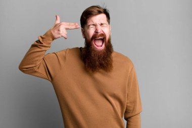 Uzun sakallı ve kızıl saçlı adam mutsuz ve stresli görünüyor, intihar jesti silah işareti yapıyor