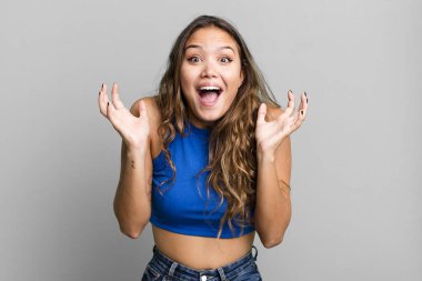 Genç ve güzel bir kadın beklenmedik bir sürpriz yüzünden şaşkın, heyecanlı, gülen, şaşkın ve mutlu hissediyor.