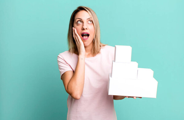 pretty blonde woman feeling happy, excited and surprised with a set of blank packagings