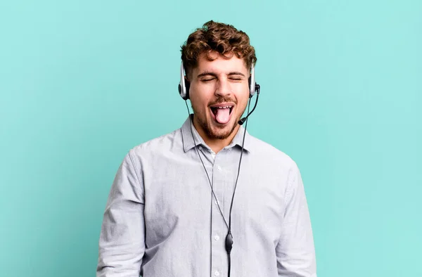 陽気で反抗的な態度を持つ若い大人の白人男性冗談と舌を突き出す テレマーケティング担当者のコンセプト — ストック写真