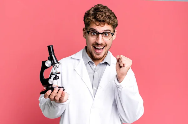 若い大人の白人男性はショックを受けて笑って成功を祝っています 顕微鏡の概念を持つ科学研究室の学生は — ストック写真