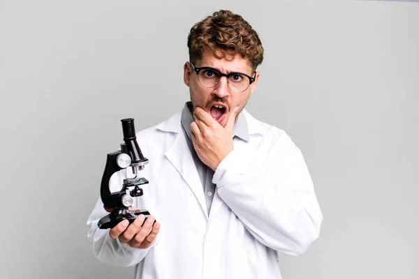 口と目を大きく開いて顎を手にした若い成人白人男性 顕微鏡の概念を持つ科学研究室の学生は — ストック写真