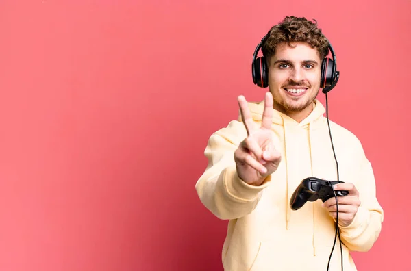 stock image young adult caucasian man smiling and looking happy, gesturing victory or peace with headset and a controller. gamer concept