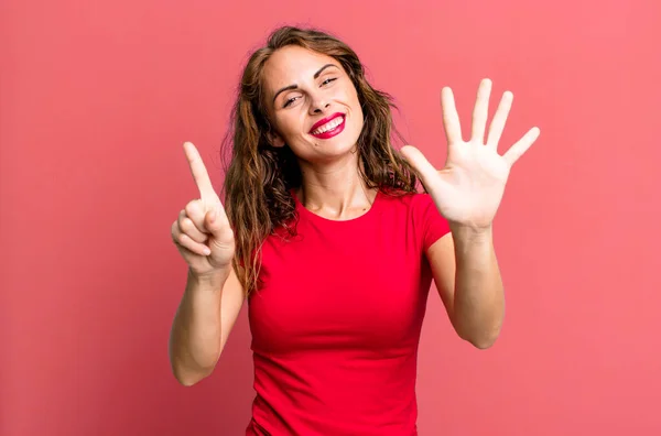 笑顔で友好的に見える若い女性が前方に手を挙げて6番目か6番目の数字を示し — ストック写真