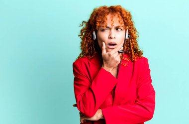 Kızıl saçlı güzel bir kadın. Ağzı ve gözleri açık ve elleri çenesinde. tele pazarlama kavramı