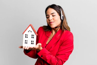 hispanic pretty young adult woman real state agent with a house model and headset