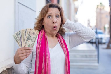 Orta yaşlı güzel bir kadın son derece şaşkın ve şaşırmış hissediyor. Dolar banknotları konsepti