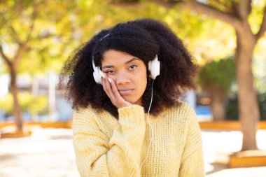 Oldukça afro siyah bir kadın bıkkın, hayal kırıklığına uğramış ve yorucu bir günün ardından uykulu hissediyor. kulaklıkla müzik dinlemek