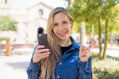 Neşeli bir şekilde gülümseyen, mutlu hisseden ve tarafını gösteren bir kadın. akıllı telefon kavramı