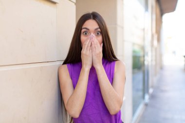 Genç ve güzel bir kadın mutlu, neşeli, şanslı ve şaşkın görünüyor. İki eliyle ağzını kapatıyor.