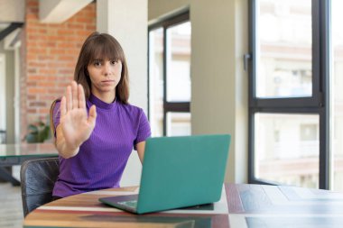 Genç ve güzel bir kadın ciddi görünüyor. Avuç içini gösteriyor. Durdurma hareketi yapıyor. masaüstü dizüstü konsepti