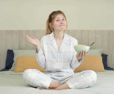 Genç, güzel bir kadın omuz silkiyor, kafası karışık ve kararsız. Kahvaltı kasesi konsepti