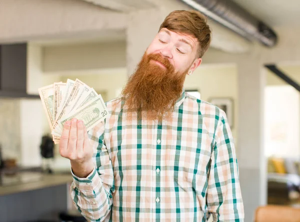 红头发的男人面带微笑 带着快乐而自信的表情看着钞票 — 图库照片
