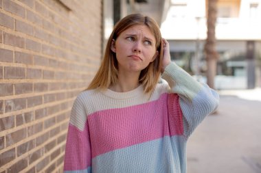 Güzel genç bir kadın şaşkın ve kafası karışmış hissediyor. Kafasını kaşıyor ve yan tarafa bakıyor.