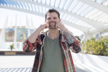 Yakışıklı adam gülümsüyor ve sahte gülüşüne işaret ediyor.