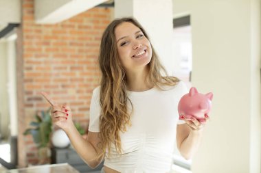 Güzel bir kadın neşeyle gülümsüyor, mutlu hissediyor ve bir tarafı işaret ediyor. Domuz kumbarası konsepti