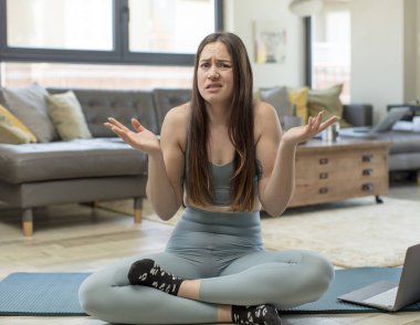 Yoga yapan genç bir kadın. Kafası karışmış ve stresli görünüyor. Farklı seçenekler arasında merak ediyor.