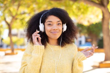 Oldukça afro siyah bir kadın omuz silkiyor, kafası karışık ve kararsız hissediyor. kulaklıkla müzik dinlemek