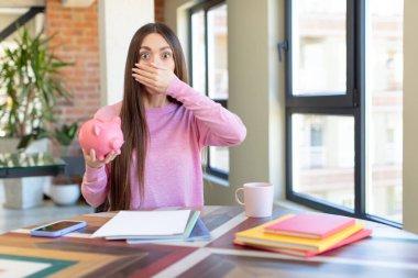 Ağzını eliyle kapatmış ve şok olmuş ya da şaşırmış bir ifade. Domuz kumbarası konsepti