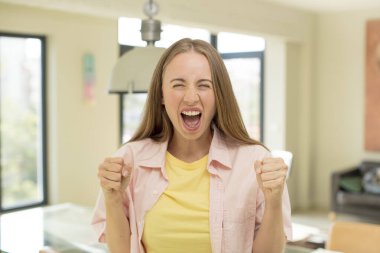 Güzel sarışın bir kadın kızgın bir ifadeyle agresif bir şekilde bağırıyor ya da yumruklarıyla başarıyı kutluyor.