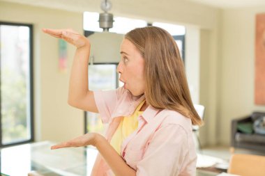 Güzel sarışın bir kadın, iki eli yanda bir objeyi tutuyor fotokopi alanında, bir objeyi gösteriyor, sunuyor ya da reklamını yapıyor.