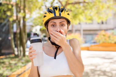 Genç ve güzel bir kadın ağzını eliyle kapatıyor ve şok olmuş ya da şaşırmış bir ifade takınıyor. bisiklet kaskı konsepti