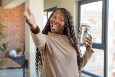 Siyah afro kadın mutlu bir şekilde gülümsüyor ve bir konsept sunuyor ya da gösteriyor. Tasarruf konseptiyle