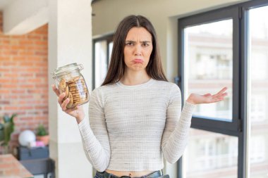 Oldukça genç bir model omuz silkiyor, kafası karışık ve kararsız hissediyor. Ev yapımı kurabiye konsepti