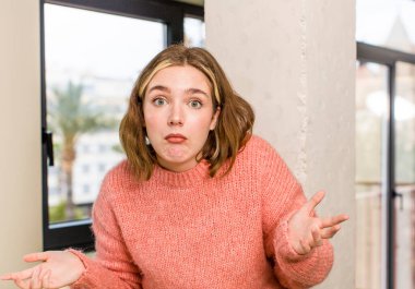 pretty caucasian woman feeling clueless and confused, having no idea, absolutely puzzled with a dumb or foolish look. home interior concept