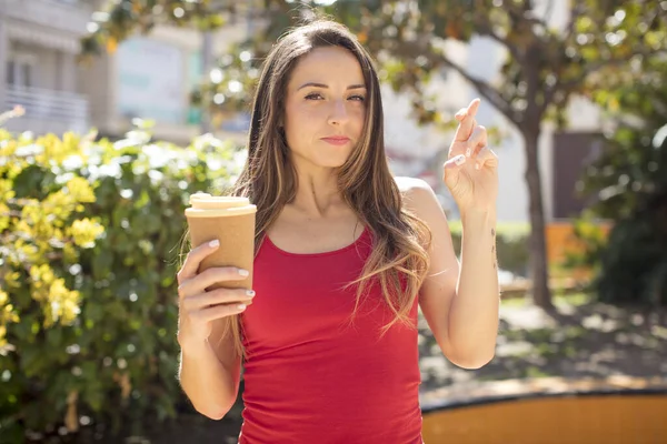 stock image pretty woman crossing fingers and hoping for good luck. take away coffee concept