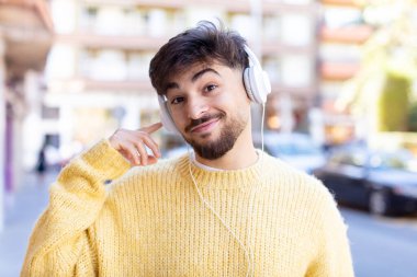 Genç ve yakışıklı bir adam gülümsüyor ve kendine güveni tam bir ifadeyle bakıyor. kulaklıkla müzik dinlemek