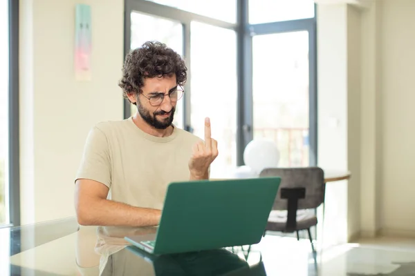 一个留着胡子的年轻人 带着笔记本电脑 感到愤怒 叛逆和好斗 扭动中指 — 图库照片