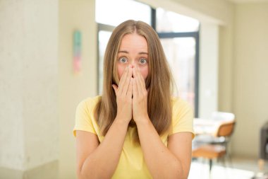 Güzel sarışın kadın mutlu, neşeli, şanslı ve şaşkın görünüyor. İki eliyle ağzını kapatıyor.