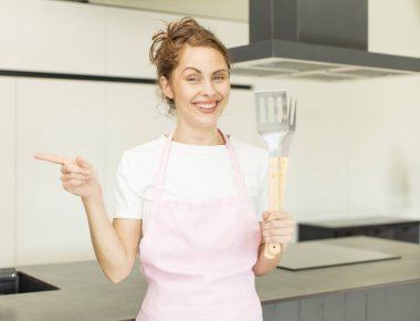 Genç, güzel bir kadın neşeyle gülümsüyor, mutlu hissediyor ve bir tarafı işaret ediyor. ev aşçısı konsepti