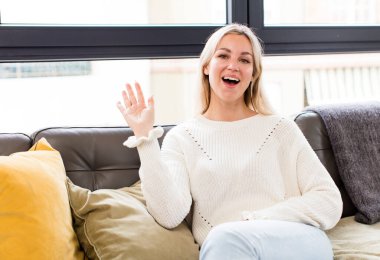 Genç, güzel bir kadın mutlu ve neşeyle gülümsüyor, el sallıyor, seni selamlıyor, ya da bir kanepede oturup veda ediyor.