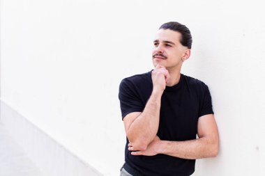 Genç havalı adam mutlu bir şekilde gülümsüyor ve hayal kuruyor ya da şüphe ediyor, yan tarafa bakıyor.