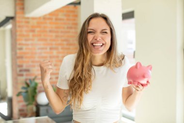 Güzel kadın şokta, gülüyor ve başarıyı kutluyor. Domuz kumbarası konsepti