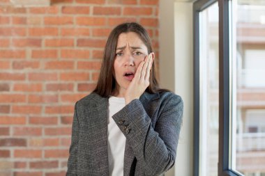 young adult pretty woman feeling shocked and astonished holding face to hand in disbelief with mouth wide open