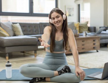 Genç yetişkin bir kadın yoga yapıyor, gülümsüyor, mutlu görünüyor, kendinden emin ve arkadaş canlısı görünüyor, bir anlaşmaya varmak için el sıkışmayı teklif ediyor, işbirliği yapıyor.