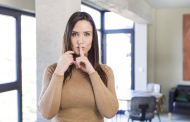 Genç ve güzel bir kadın ciddi görünüyor ve parmaklarını dudaklarına bastırıp sessizlik ya da sessizlik talep ediyor, sır saklıyor.