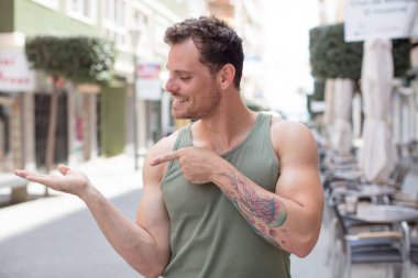 Yakışıklı adam gülümsüyor, mutlu, kaygısız ve tatmin olmuş hissediyor, fotokopi alanındaki konsepte ya da fikre işaret ediyor.
