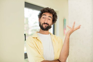 Genç, çılgın, sakallı, gururla gülümseyen, mutlu ve memnun hisseden ve fotokopi alanında bir konsept gösteren bir adam.