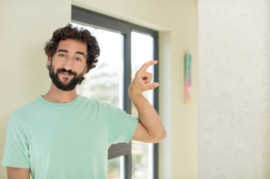 Genç çılgın sakallı adam elinde bir nesne tutuyor, küçük bir şey gösteriyor, sunuyor ya da reklamını yapıyor.