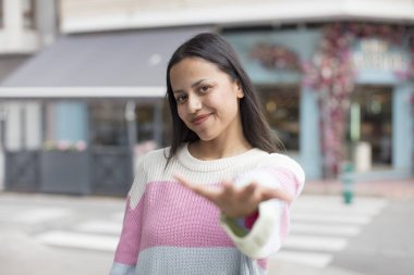 Güzel İspanyol bir kadın gülümsüyor, mutlu, kendinden emin ve arkadaş canlısı görünüyor, bir anlaşmaya varmak için el sıkışmayı teklif ediyor, işbirliği yapıyor.