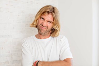 Genç sarışın bir adam hayal kırıklığına uğramış ve hayal kırıklığına uğramış hissediyor. Ciddi görünüyor, kızgın ve kollarını kavuşturmuş.