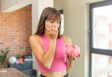 Genç, güzel bir kadın korkmuş, endişeli ya da kızgın hissediyor ve domuz kumbarası konseptine bakıyor